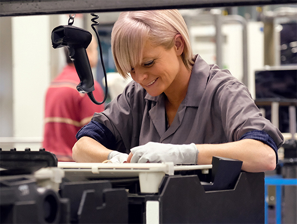 In an Apple manufacturing facility, two employees examine aluminium MacBook shells on titanium anodising racks.