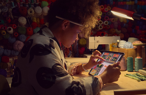 En person, der sidder ved et skrivebord, bruger to fingre på skærmen på en iPad til at zoome ind på et billede.