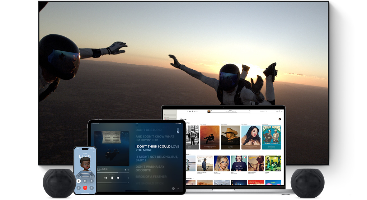 Geniş düz ekran bir televizyon gösteriliyor. Televizyonun önünde yan yana dizilmiş şekilde bir MacBook Pro, bir iPad, bir iPhone ve Gece Yarısı renginde bir HomePod mini yer alıyor.