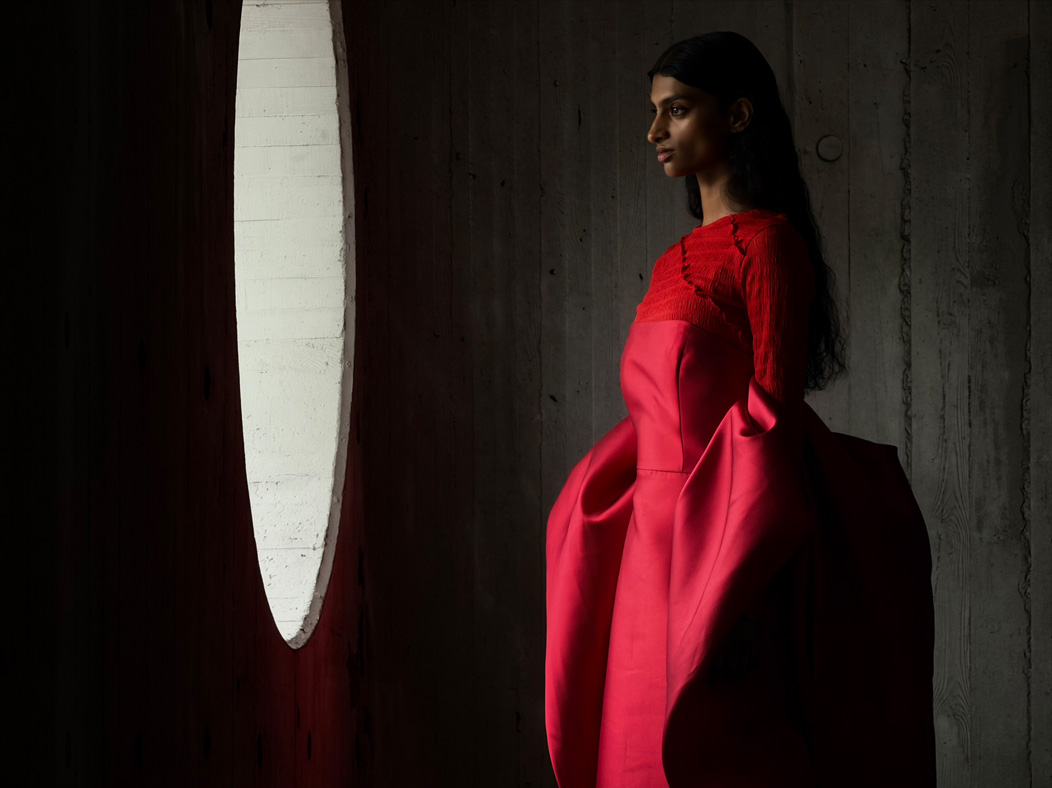 A woman wearing a long red dress stands in an empty room being photographed. The Photo app toggles through the following focal lengths to demonstrate the capabilities of the pro camera system: 200 mm, 100 mm, 48 mm, 35 mm, 28 mm, 13 mm, and macro