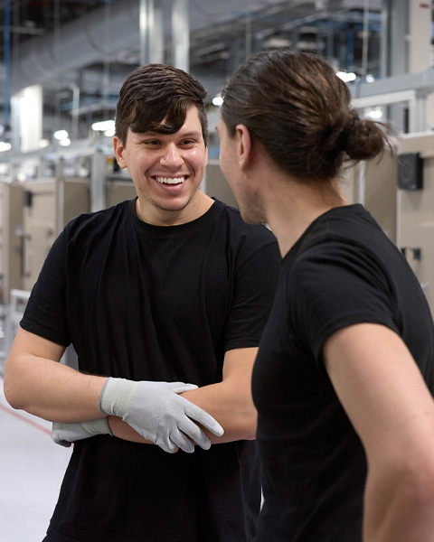 Two employees in an iMac assembly warehouse talk with each other